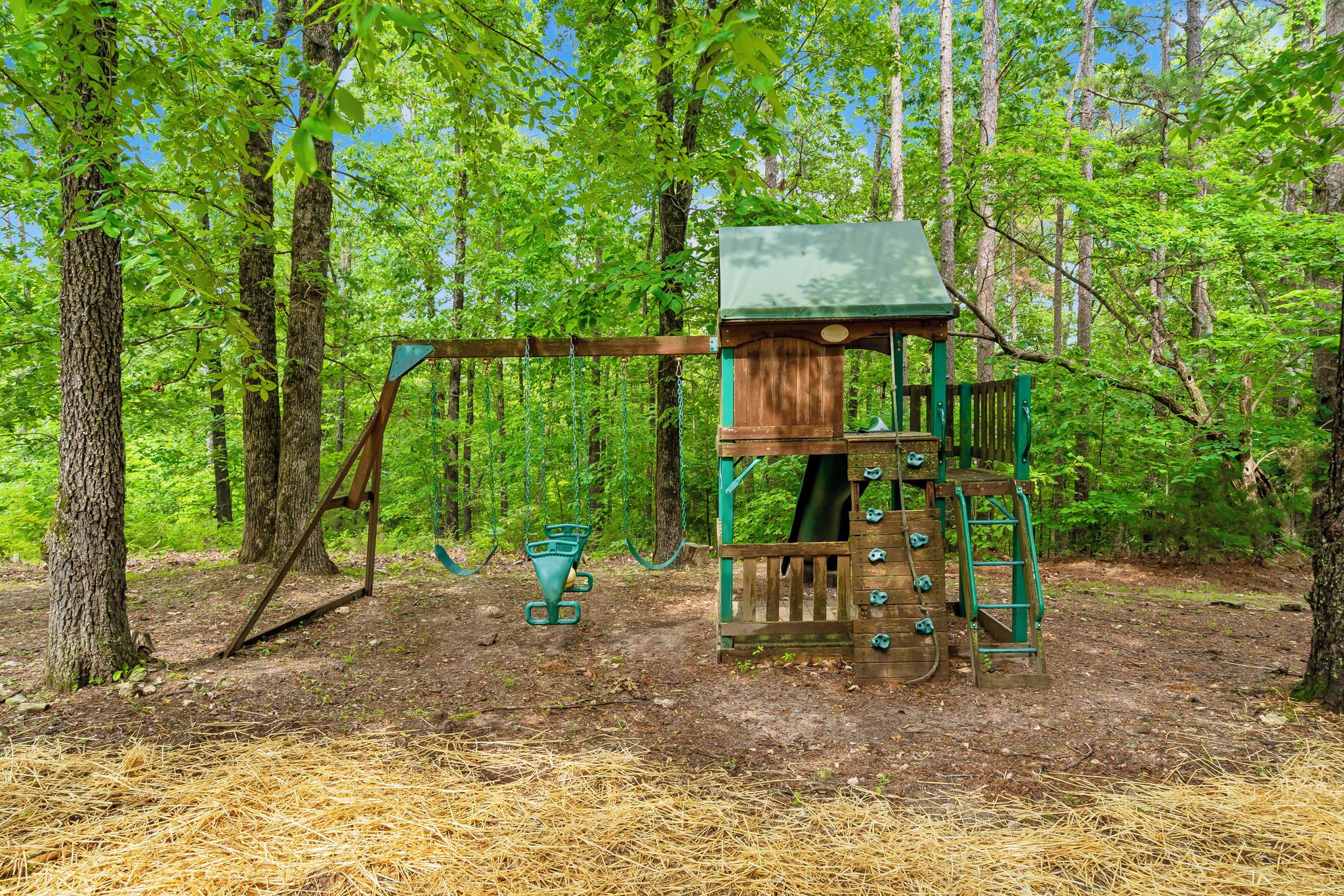 A wooden play structure with a swing set and climbing elements in a forested area.