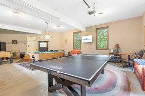 A spacious living room with a ping pong table, pool table, and a billiards table. There is a television mounted on the wall and a window providing natural light. - Secluded 40 Acres Near Table Rock, Stunning Views, Games, Community Pool & Car Charger (Blue Eye)