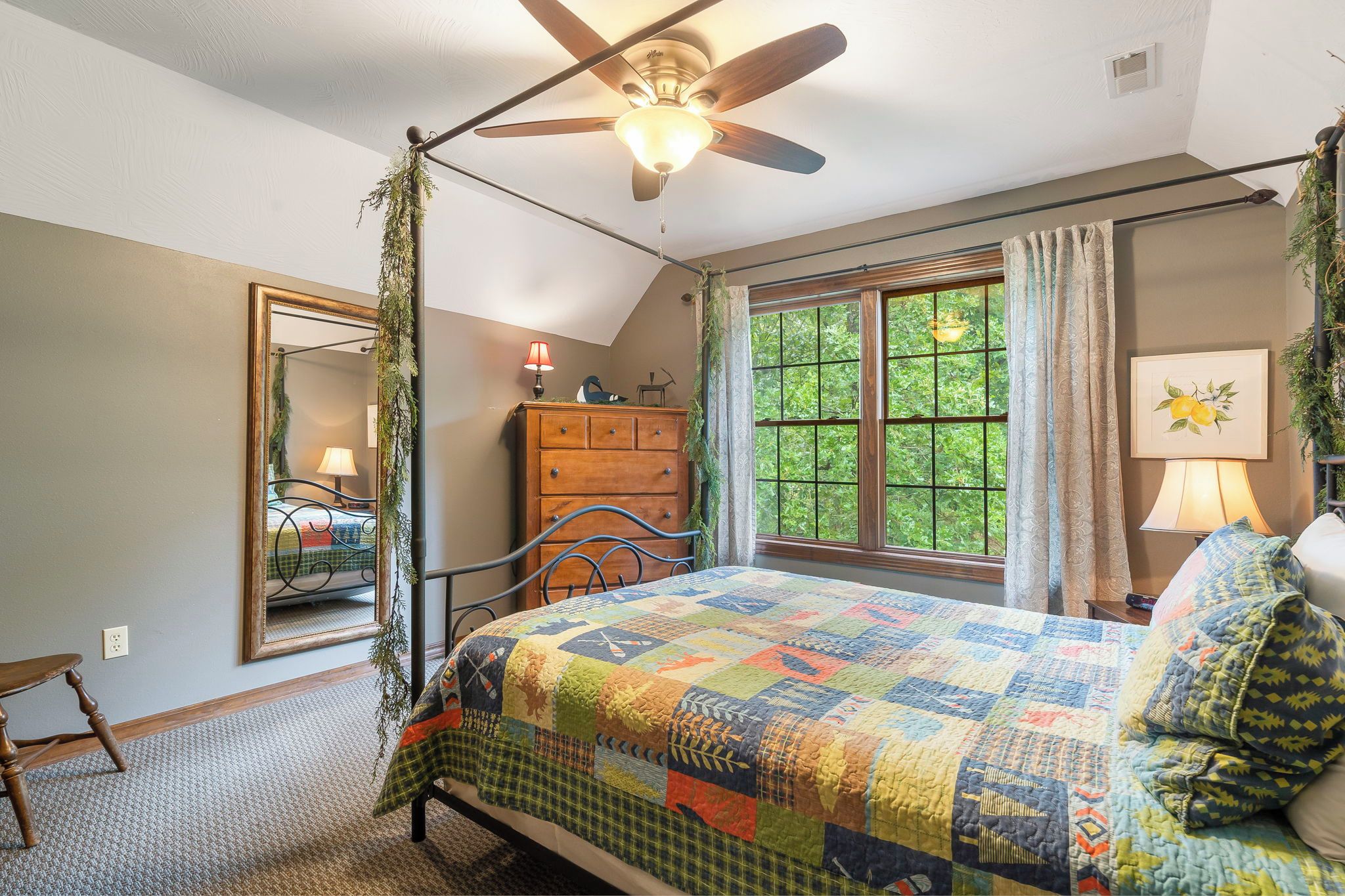 A bedroom with a bed, a dresser, a mirror, a window with curtains, and a ceiling fan.