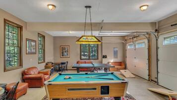A pool table in a room with a ceiling light, a sofa, and a table with chairs.