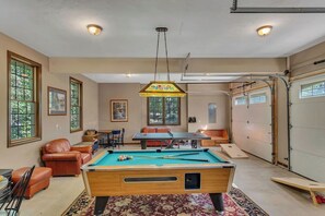 Ein Billardtisch in einem Raum mit Deckenleuchte, einer Couch und einem Tisch mit Stühlen.