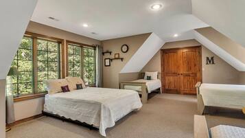 A bedroom with a large window, a bed, a nightstand, a wooden door, and a letter 'M' on the wall.