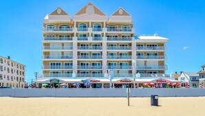 A multi-story hotel with balconies, located near a beach with outdoor dining areas.