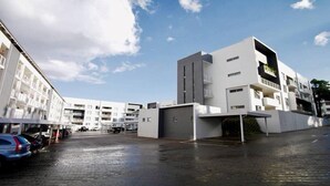 Un edificio moderno con tetto piatto, diversi balconi e un'area di parcheggio antistante.