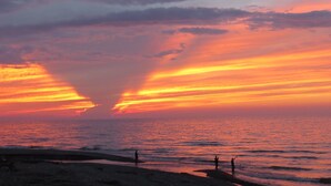 Una playa al atardecer con siluetas de personas y un cielo despejado.