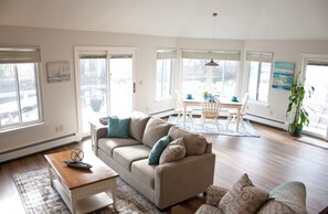 A spacious living room with a beige sofa, a wooden coffee table, and a dining area with a table and chairs.