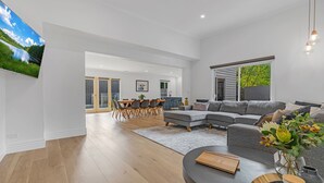 Ein modernes Wohnzimmer mit einem grauen Ecksofa, einem runden Couchtisch und einem an der Wand befestigten Flachbildfernseher.