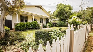Ein zweistöckiges Haus mit Veranda, umgeben von einem gepflegten Garten und einem weißen Zaun.