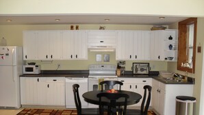 A compact kitchen with white cabinets, a dining table with chairs, a microwave, a stove, and a trash can. - Cozy Cottage with 45' Lake Frontage and Kayaks (Lodi)