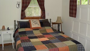 A bedroom with a bed, a nightstand, a lamp, a window with curtains, and a door. - Cozy Cottage with 45' Lake Frontage and Kayaks (Lodi)