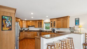 A modern kitchen with wooden cabinets, a central island with stools, and a refrigerator. - Mountain to Sea - Direct Beach Access -Ocean Views - 4BD +Bonus Bedroom (Folly Beach)