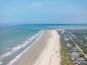 Une vue aérienne d’une plage avec une longue étendue de sable, quelques personnes et des maisons le long du rivage.
