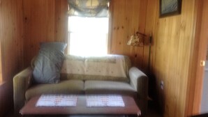 Un interior de madera con un sofá, una mesa con papeles y una ventana con cortina.