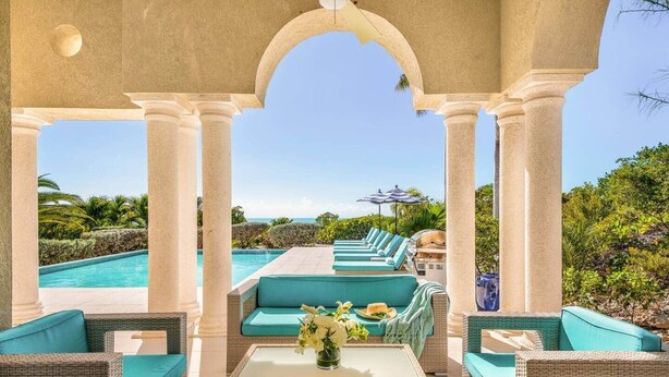 Ein Poolbereich mit Korbmöbeln, einem Glastisch und Blick auf Pool und Grünflächen.