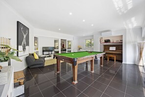 Un salon moderne avec une table de billard, un canapé, un téléviseur et un piano.