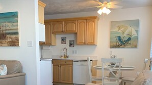 A modern living room with a beige sofa, wooden flooring, and a kitchen area with wooden cabinets and a dishwasher. - Great Location ! 1 Short Block To The Boardwalk. (Virginia Beach)