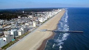 An aerial view of a coastal city with a long beach, a pier extending into the ocean, and dense urban development along the shoreline. - Great Location ! 1 Short Block To The Boardwalk. (Virginia Beach)