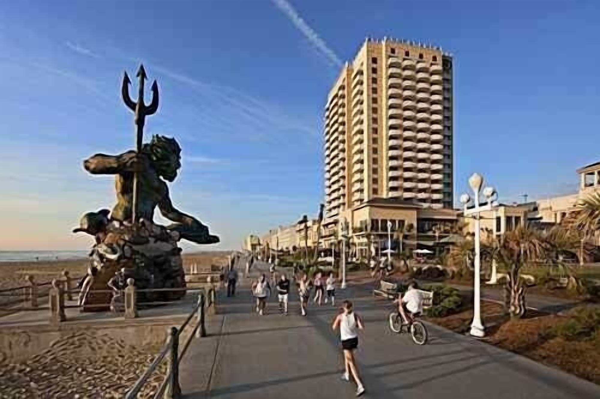 A coastal promenade with a large statue, a tall hotel, and a clear sky.