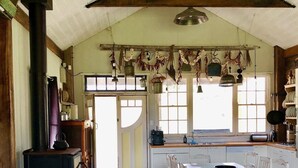 Een rustieke keuken met een houtkachel, een lange eettafel en hangende decoraties.