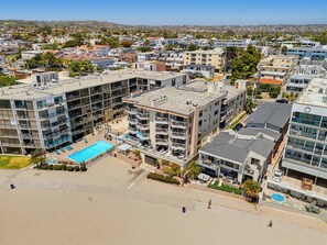 A multi-story hotel with a rooftop pool, surrounded by residential buildings and a beach.