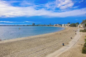 A beach with a clear sky, a sandy shore, and a few buildings in the background.