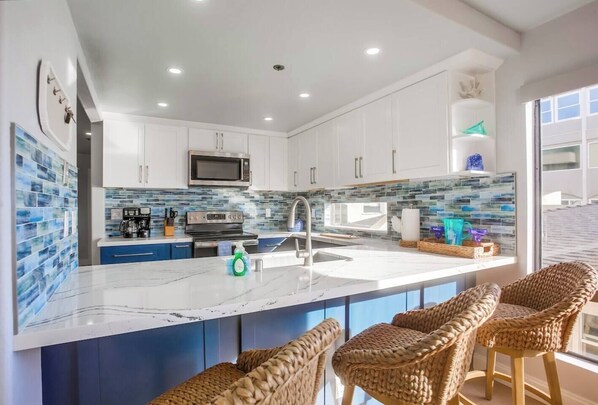 A modern kitchen with white cabinets, a marble countertop, and a built-in microwave.