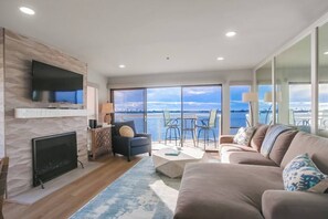 A modern living room with a flat-screen TV, a fireplace, a sofa, and a view of the water.