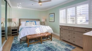 Un dormitorio con cama, mesitas de noche, un banco, cómoda y ventana con persianas.