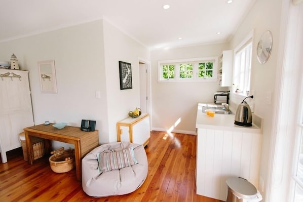 Un espace de vie compact comprenant un coin cuisine, un coin repas avec une table et un banc en bois, et un petit coin salon.