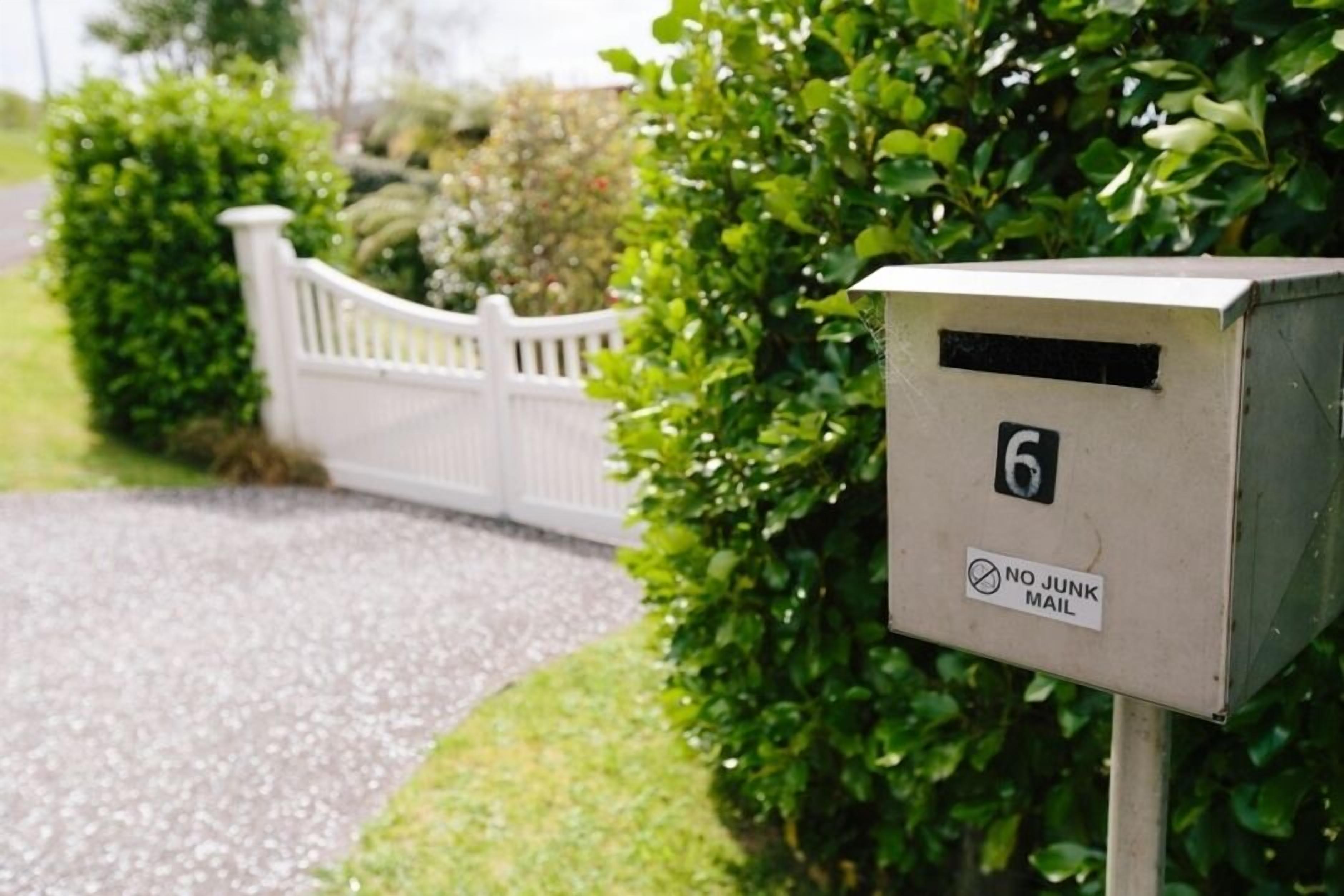 A mailbox with a 'NO JUNK MAIL' sign, number 6, and a white picket fence in the background.