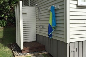 A small, enclosed outdoor shower area with a wooden deck and a towel hanging on the wall.