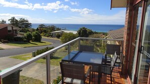 A balcony with a table and chairs, overlooking a street and a body of water. - Tura Views, 3 BR House (Tura Beach, Merimbula)