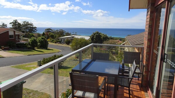 A balcony with a table and chairs, overlooking a street and a body of water.