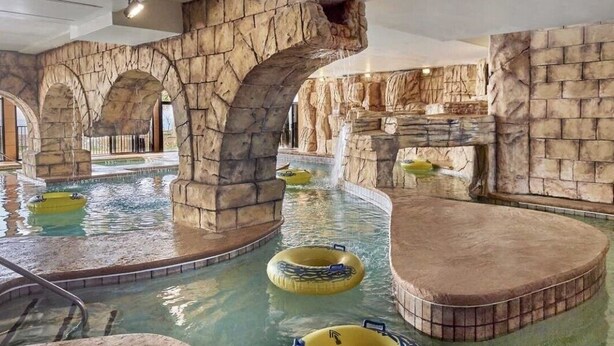 Parque acuático interior con formaciones rocosas artificiales, una piscina y flotadores inflables.