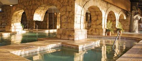 An indoor swimming pool with stone arches and a stone wall.