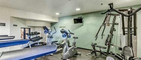 A gym with cardio equipment, weight machines, and a bench.