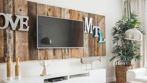 Una sala de estar moderna con una pared de acento de madera, televisor de pantalla plana, mobiliario blanco y una planta en maceta.