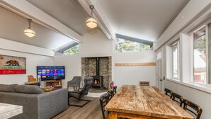 A modern living room with a fireplace, a large wooden dining table, and a gray sofa. - Lily Pad_Modern w/ AC! + Games, Smart TV's & HOA Amenities (Gym/HotTub/Sauna/Pool) (Truckee)