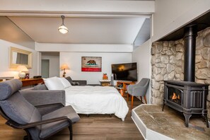 Une chambre moderne avec un lit, deux fauteuils, un téléviseur, une cheminée et un mur en pierre.