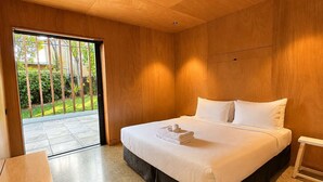 Quarto moderno com cama grande, piso de madeira e porta de vidro deslizante para um jardim.