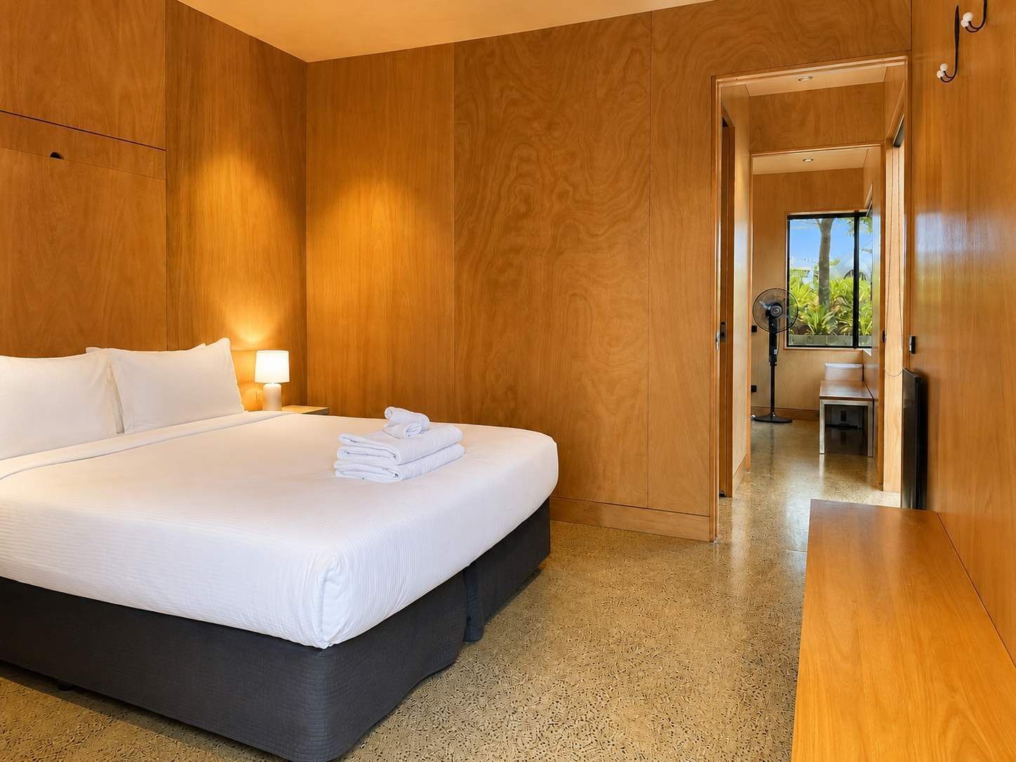 Ein Hotelzimmer mit einem großen Bett, Holzwänden, einem Nachttisch mit Lampe und Blick durch eine offene Tür.