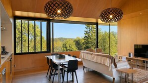 Um interior moderno com área de jantar, sofá, TV e grandes janelas com vista para árvores.