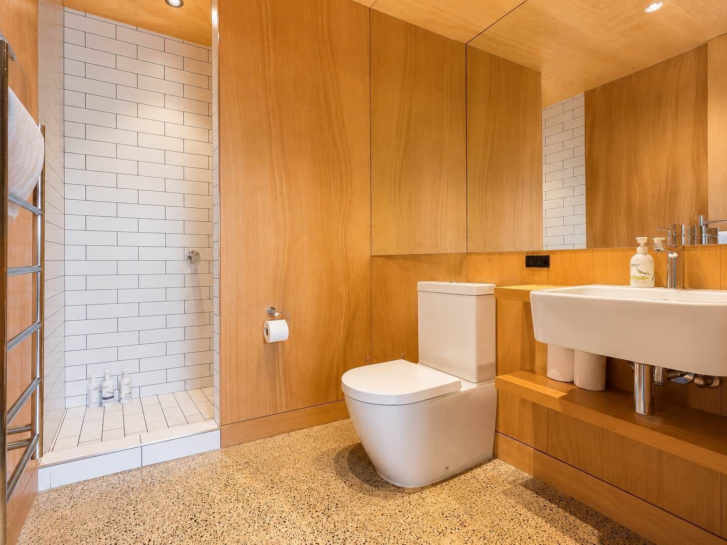 Un baño moderno con ducha, inodoro y lavamanos, con muebles de madera y azulejos blancos.