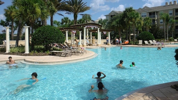 A swimming pool with people enjoying the water, surrounded by palm trees and a covered pavilion. - Newly Updated, 6BR Villa, South Facing Pool, Free water park (Kissimmee)