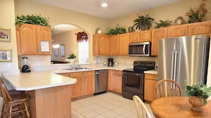 A kitchen with wooden cabinets, a stainless steel refrigerator, a microwave, and a dishwasher. - Newly Updated, 6BR Villa, South Facing Pool, Free water park (Kissimmee)