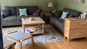 A living room with two grey sofas, a wooden coffee table, a patterned rug, and a wooden chest of drawers.