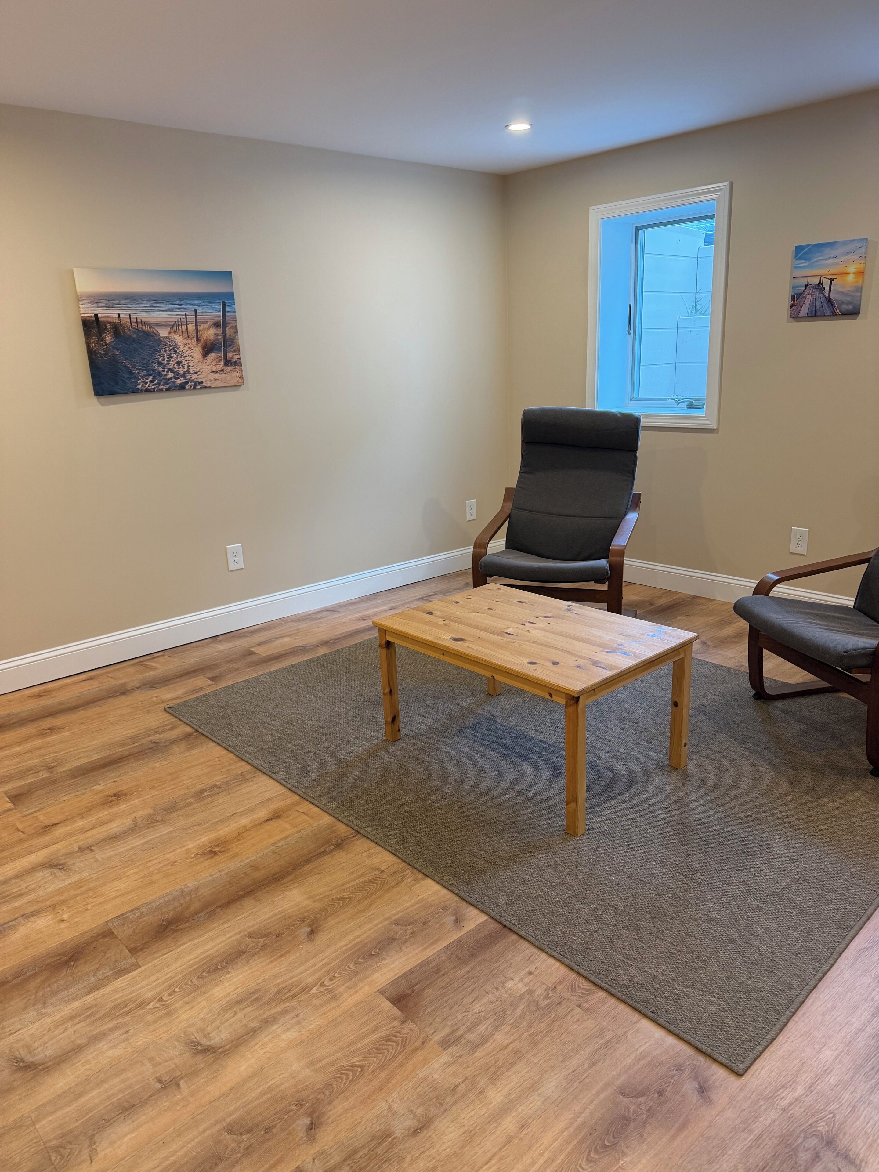A room with a wooden floor, a grey rug, a wooden coffee table, and two chairs.