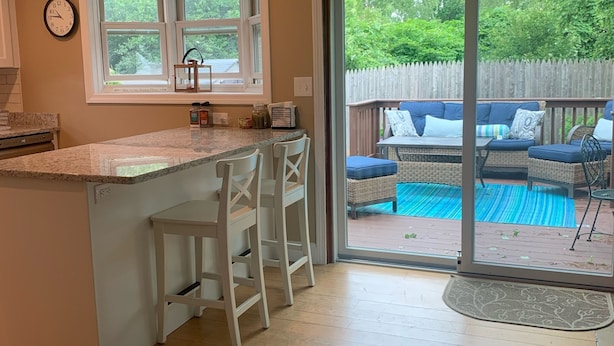 A kitchen with a large island, a dining area with white chairs, and a view of a backyard with a pool and outdoor furniture.