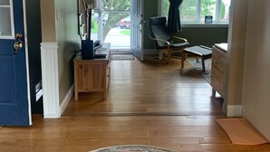 A spacious living room with hardwood flooring, a large rug, a blue door, and a view of the outside through a glass door.