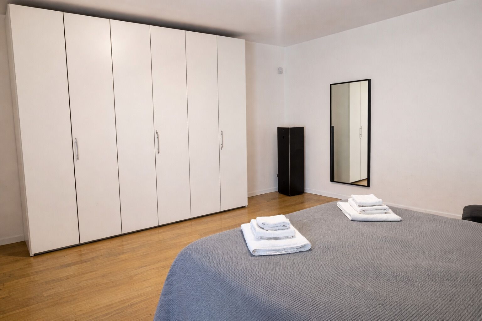 Un dormitorio con un armario grande, una cama con colcha gris y un altavoz negro.